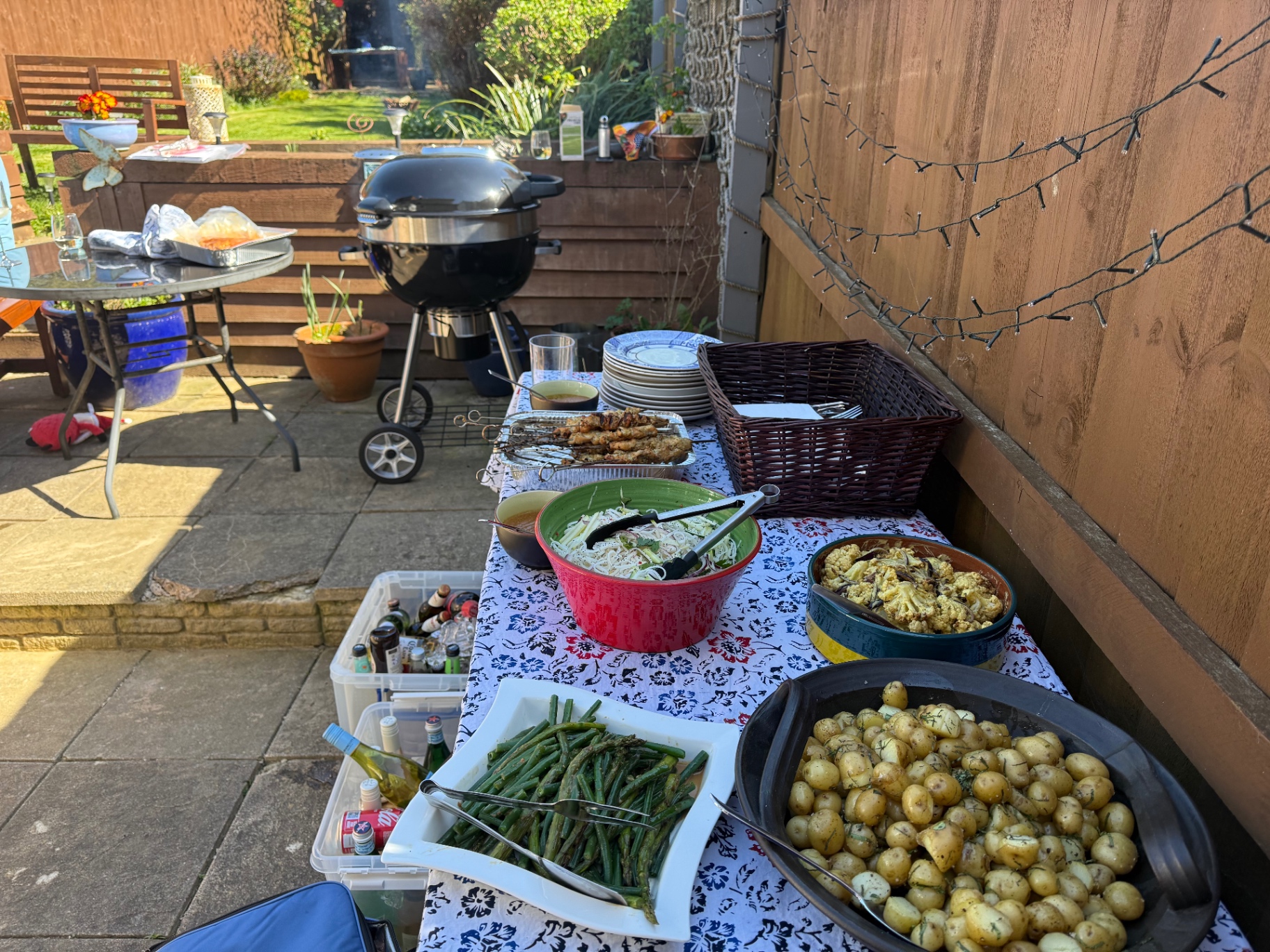 Outdoor BBQ buffet table with chargrilled skewers, dill new potatoes, grilled asparagus, spiced cauliflower and Vietnamese rice-noodle salad beside a Weber kettle in a Bristol garden — Lovey Chef private BBQ catering